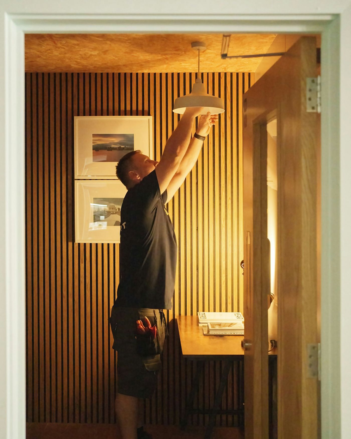 An electrician fitting a pendant light in a timber-lined room
