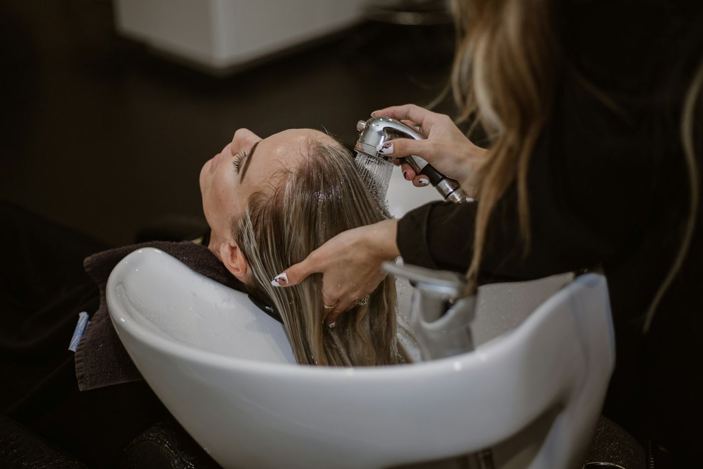 A stylist rinsing a client's hair at the basin